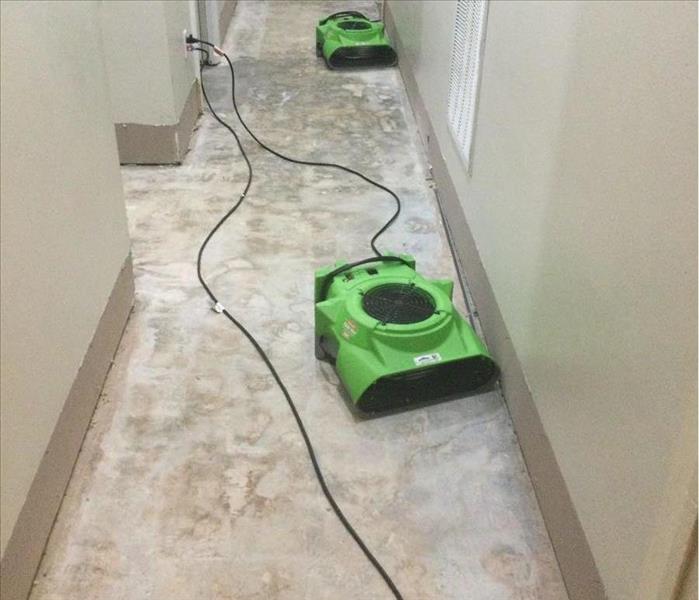 hallway in home without flooring with two green air movers pointed at drywwall