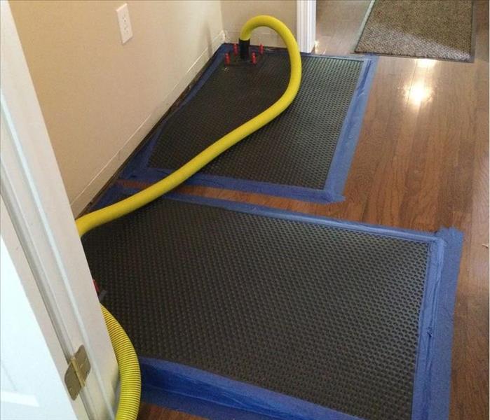 black mats on top of wood flooring with yellow hose connected to them to dry floors