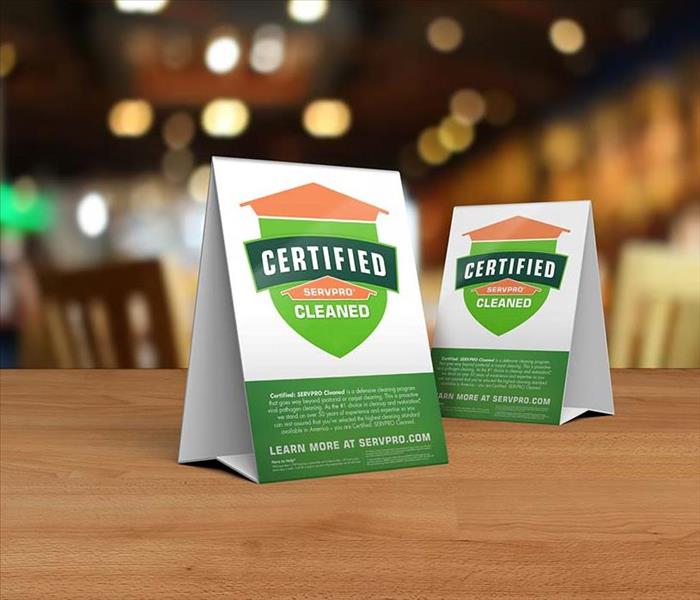 Table tent signs describing the Certified: SERVPRO Cleaned program on top of a wooden table.